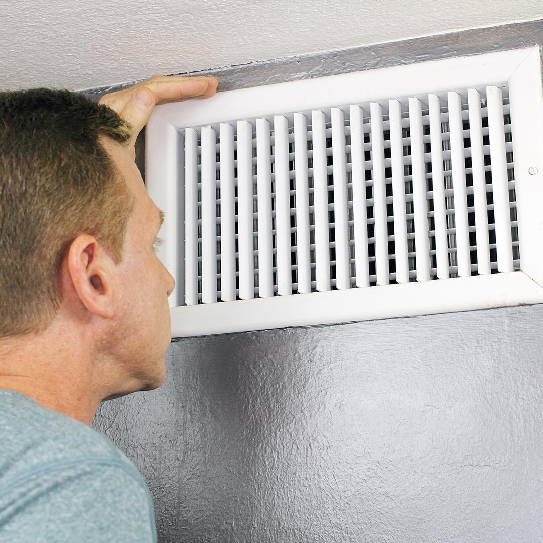 Man checking air vent in home