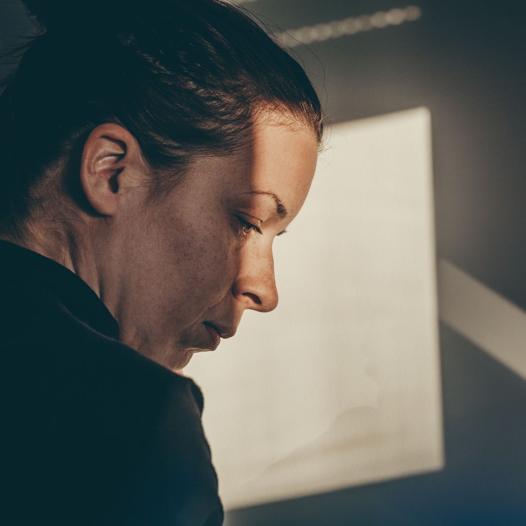 woman looks down with light from window half shining on her face 